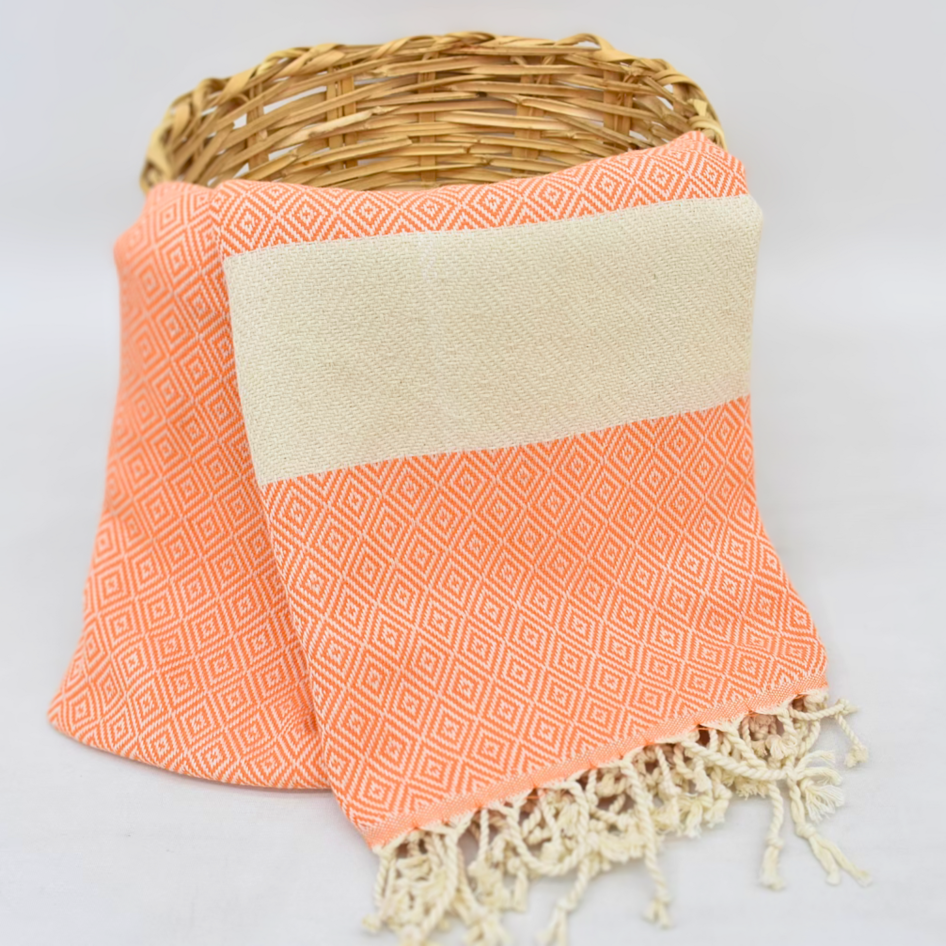 Turkish towel with an orange diamond pattern and natural color stripes hanging from a basket, embodying autumn warmth and elegance with hand-tied knots