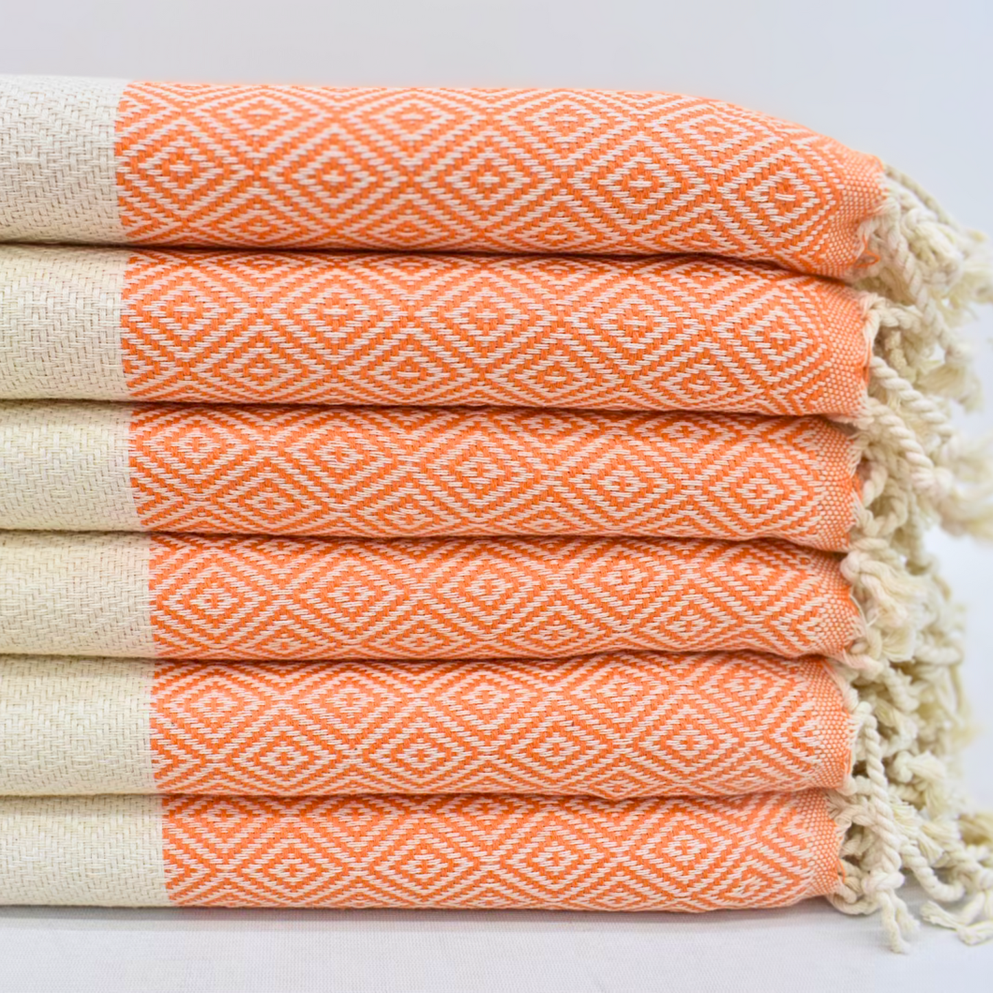 Stack of folded Turkish towels featuring orange diamond patterns and natural color stripes, topped with hand-tied knots, exuding autumnal elegance