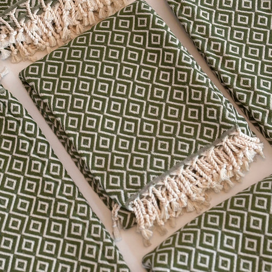 Green and white patterned folded THYME Peshtemal Towels with fringes on a white background