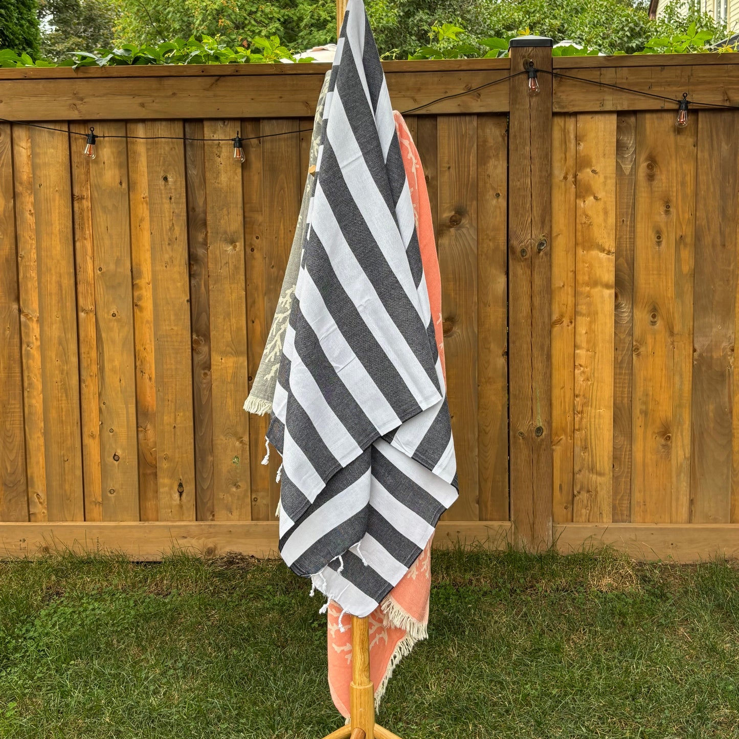 Black and white striped Turkish  towel draped over a wooden rack with trees and grass in the background