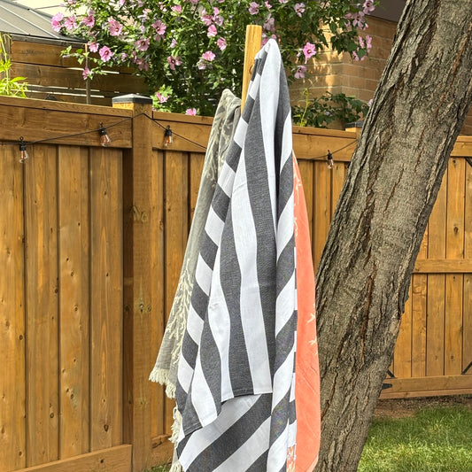 Black and white Turkish towel striped towel draped over a wooden deck with a tree and grass in the background.