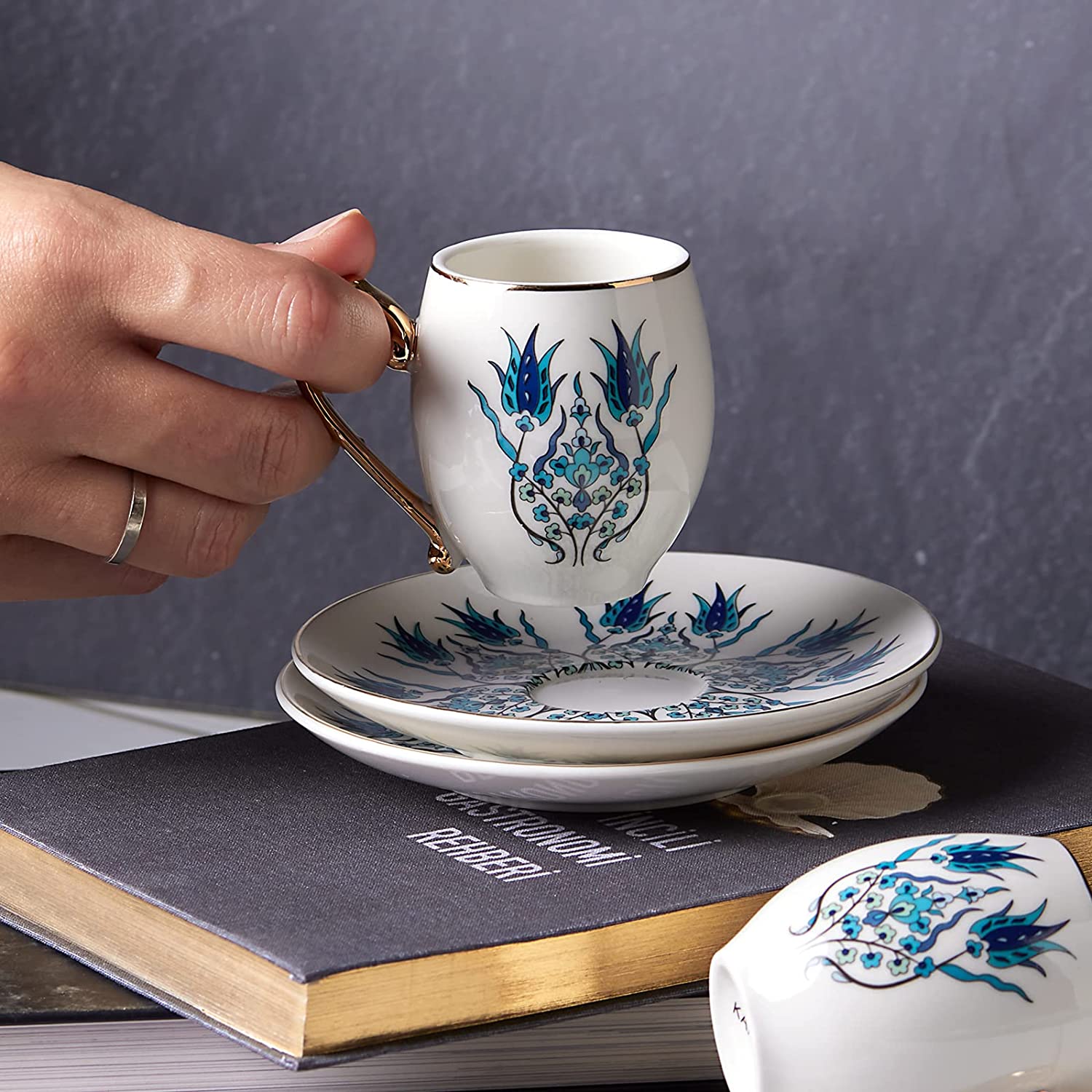 Woman's hand holding IZNIK Turkish Coffee Cup on a book
