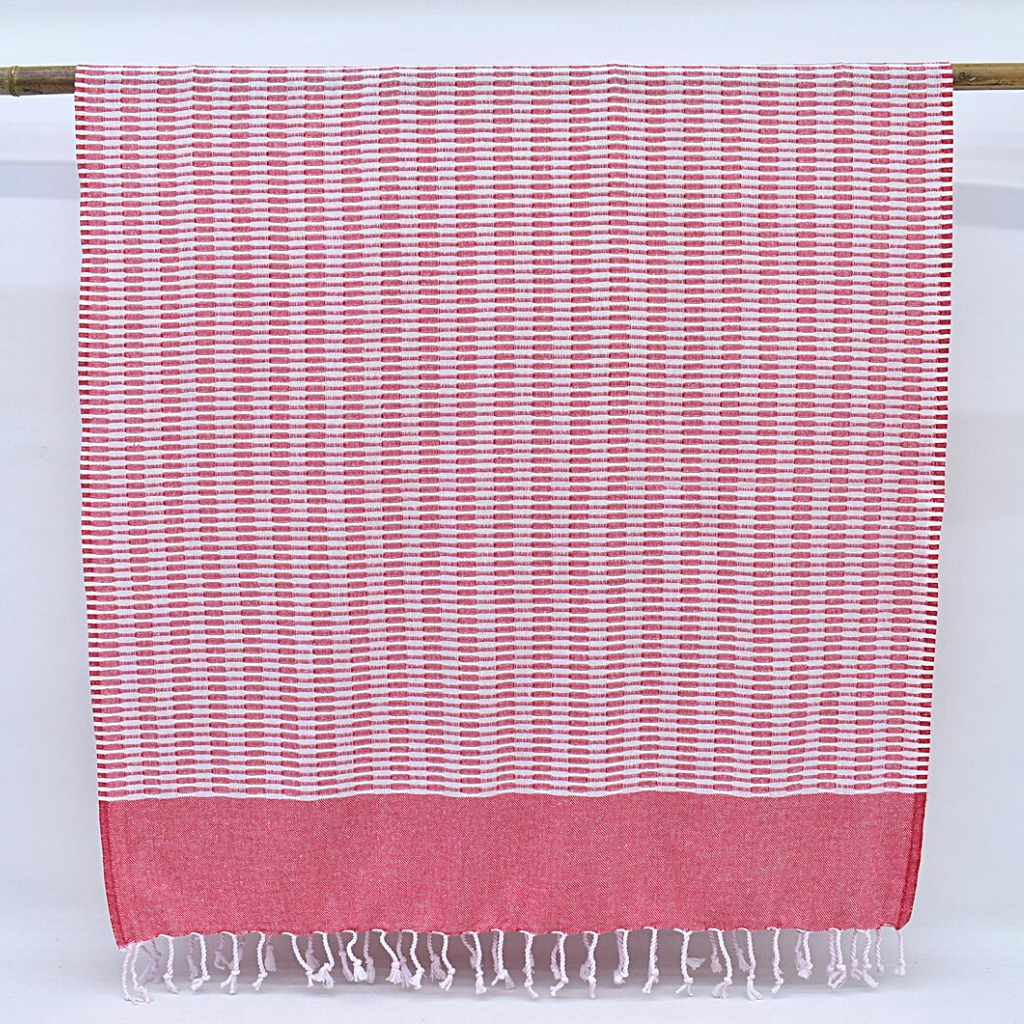 Red and white striped hanging Turkish towel with tasseled bottom against a white wall
